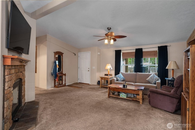 carpeted living area with a stone fireplace and a ceiling fan