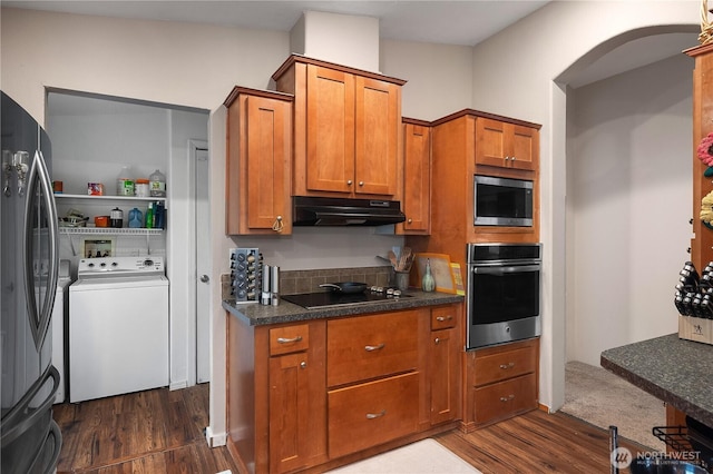 kitchen with dark wood-style floors, stainless steel appliances, brown cabinetry, washer / dryer, and under cabinet range hood