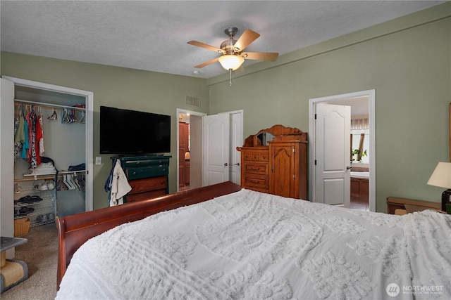 bedroom with a textured ceiling, visible vents, vaulted ceiling, carpet, and a walk in closet