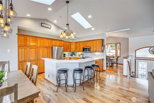 kitchen with brown cabinets, a spacious island, appliances with stainless steel finishes, light wood-type flooring, and vaulted ceiling with skylight