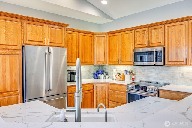 kitchen with light stone counters, brown cabinets, stainless steel appliances, lofted ceiling, and decorative backsplash