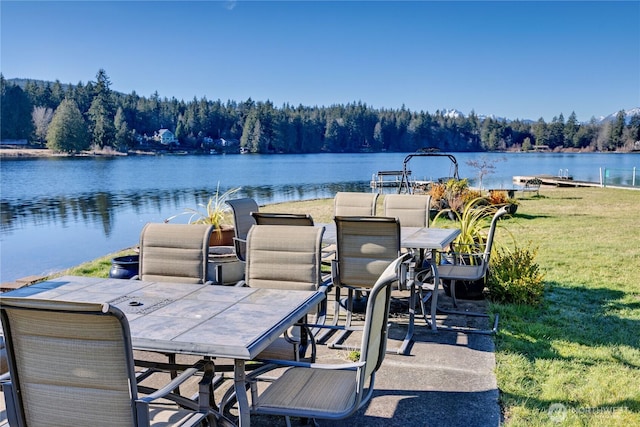 view of patio / terrace with outdoor dining space, a water view, and a wooded view