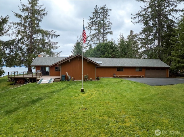 back of property with an attached garage, aphalt driveway, and a lawn