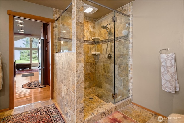 full bathroom featuring stone tile floors, a shower stall, and baseboards