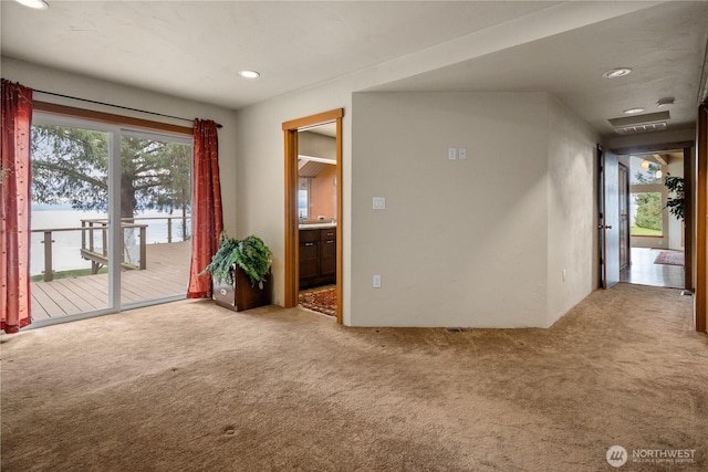 carpeted empty room with a water view, visible vents, and recessed lighting