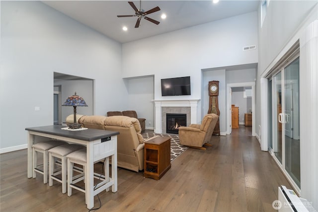 living room with hardwood / wood-style floors, a high ceiling, a tile fireplace, and visible vents