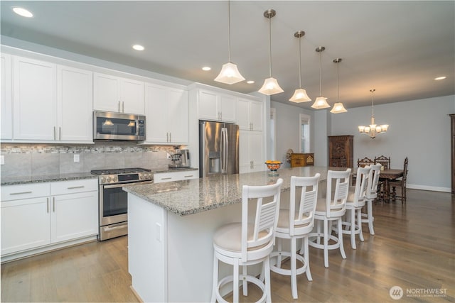 kitchen featuring stainless steel appliances, wood finished floors, a kitchen island, white cabinets, and tasteful backsplash