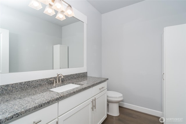 bathroom with toilet, vanity, wood finished floors, a chandelier, and baseboards