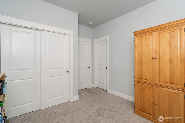 unfurnished bedroom featuring baseboards, a closet, and light colored carpet