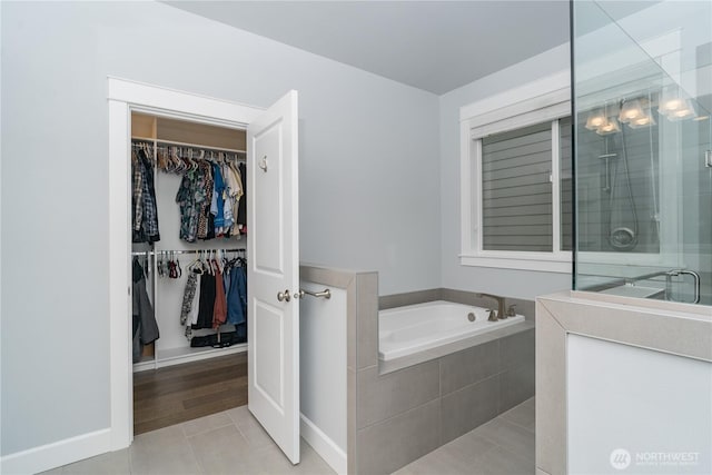 full bath featuring a stall shower, a walk in closet, tile patterned flooring, and a garden tub