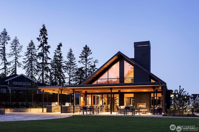 back of house featuring a lawn, a chimney, an outdoor kitchen, and a patio