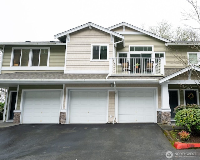 view of front of property featuring an attached garage, a balcony, stone siding, driveway, and roof with shingles