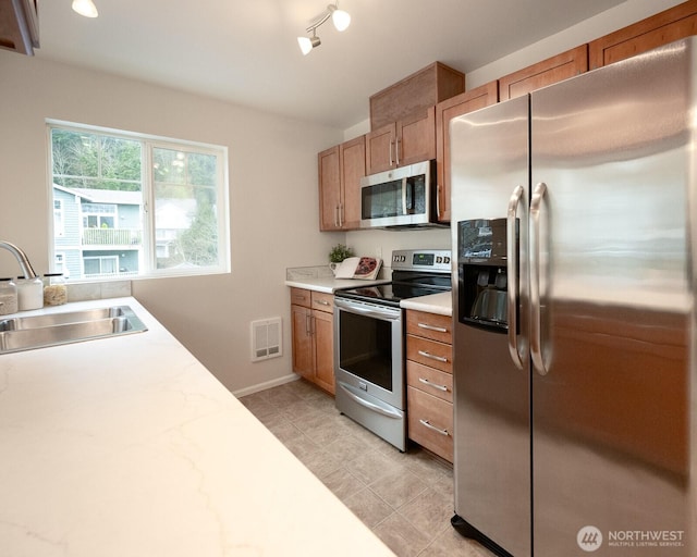 kitchen featuring stainless steel appliances, visible vents, brown cabinetry, a sink, and baseboards