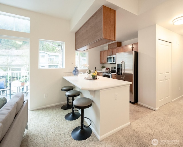 kitchen featuring stainless steel appliances, a peninsula, open floor plan, light countertops, and a kitchen bar