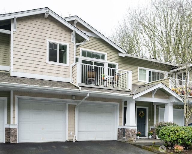 view of front of property featuring roof with shingles, a balcony, a garage, stone siding, and driveway