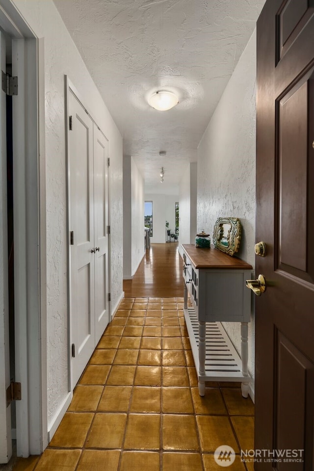 hall with tile patterned flooring, a textured wall, and a textured ceiling