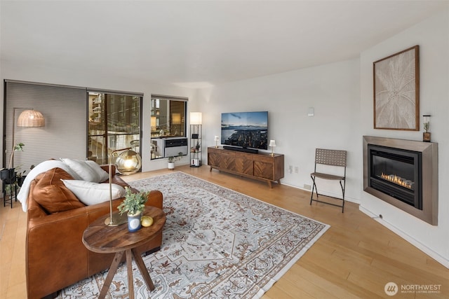 living room featuring light wood-type flooring, baseboards, and a glass covered fireplace