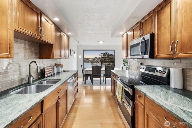 kitchen featuring light stone counters, a sink, appliances with stainless steel finishes, brown cabinets, and light wood finished floors