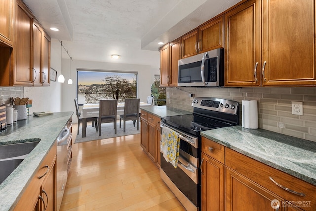 kitchen featuring stainless steel appliances, light stone counters, and brown cabinetry