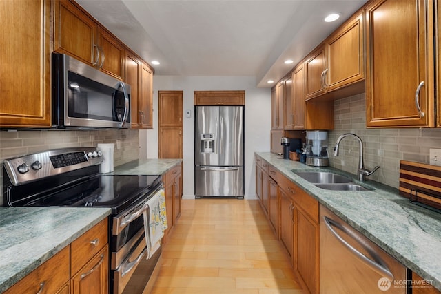 kitchen with brown cabinets, appliances with stainless steel finishes, light wood-style floors, a sink, and light stone countertops