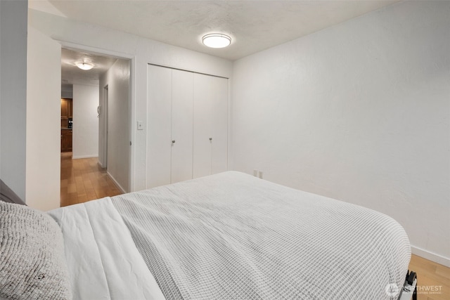 bedroom featuring light wood-type flooring, baseboards, and a closet