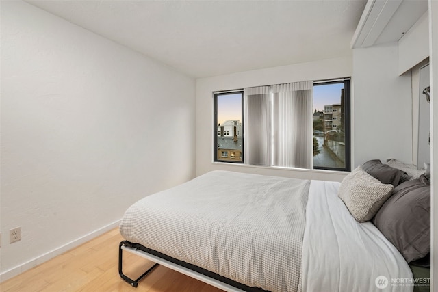 bedroom with multiple windows, baseboards, and wood finished floors