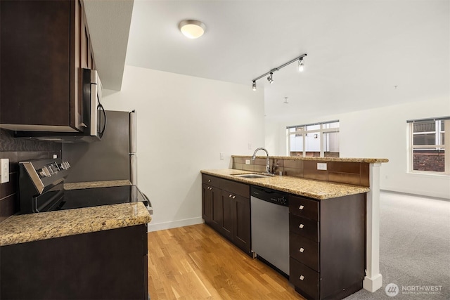 kitchen with dark brown cabinetry, stainless steel appliances, a peninsula, a sink, and light wood finished floors