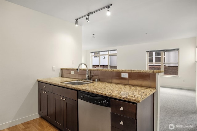 kitchen with dark brown cabinetry, a sink, light stone countertops, dishwasher, and a peninsula