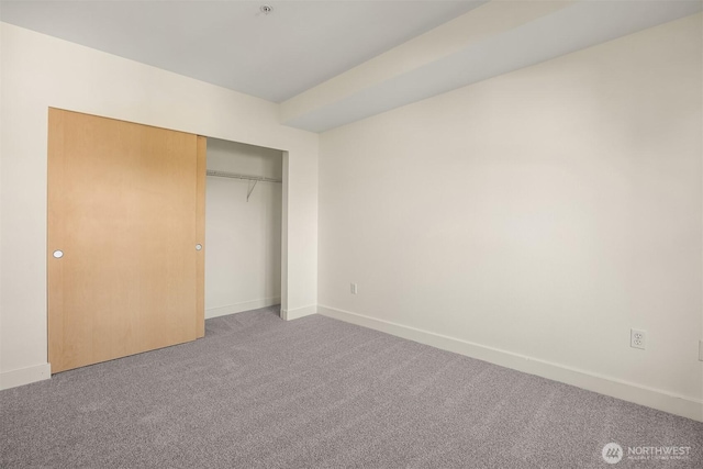 unfurnished bedroom with a closet, light colored carpet, and baseboards