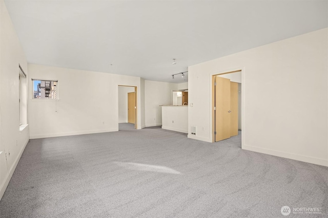 unfurnished living room featuring rail lighting, baseboards, and carpet flooring