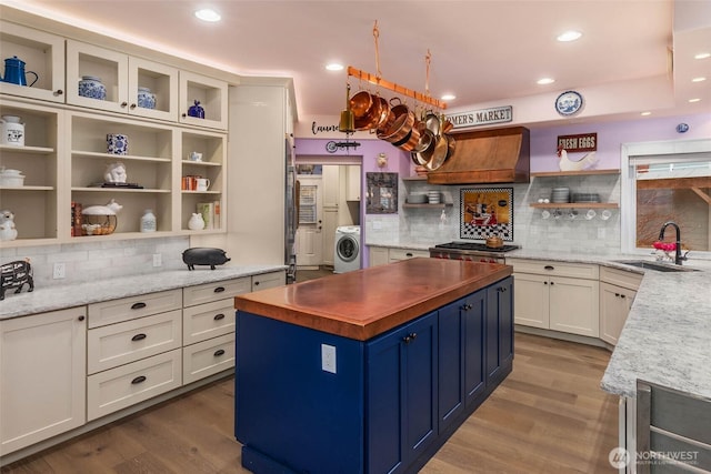 kitchen with open shelves, custom range hood, a sink, wood finished floors, and washer / dryer