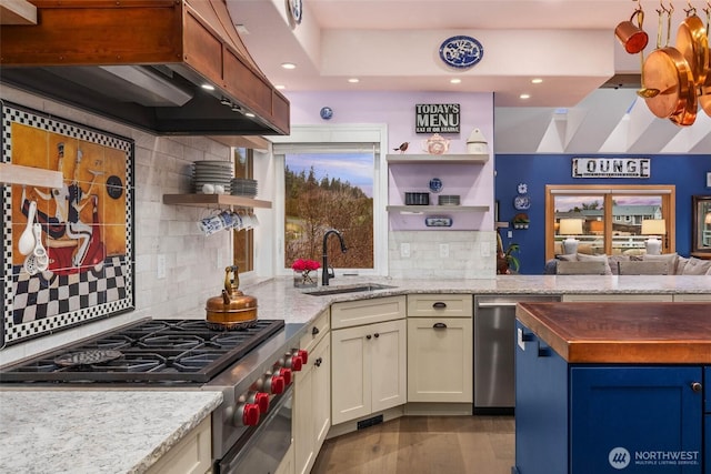 kitchen featuring open shelves, recessed lighting, custom range hood, appliances with stainless steel finishes, and a sink