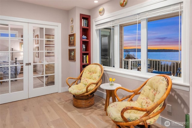 sitting room featuring a water view, baseboards, wood finished floors, and french doors