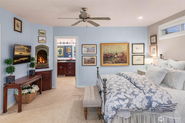 bedroom with light colored carpet, connected bathroom, a sink, ceiling fan, and baseboards