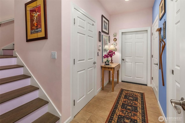 entryway featuring light tile patterned flooring, baseboards, and stairs