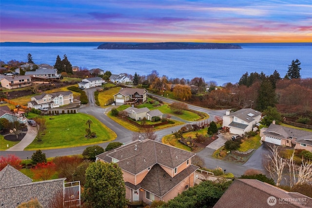 aerial view at dusk with a water view and a residential view