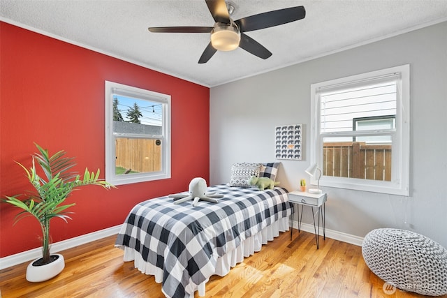 bedroom featuring ceiling fan, baseboards, light wood-type flooring, and a textured ceiling