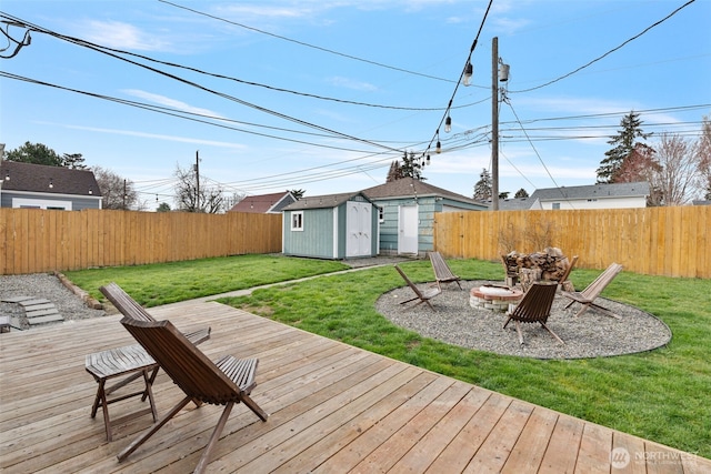 wooden terrace featuring an outdoor structure, a fenced backyard, a shed, and an outdoor fire pit