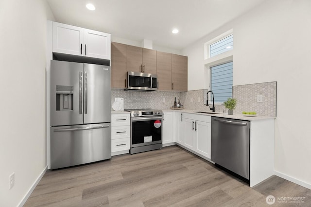 kitchen featuring light countertops, decorative backsplash, appliances with stainless steel finishes, white cabinets, and a sink