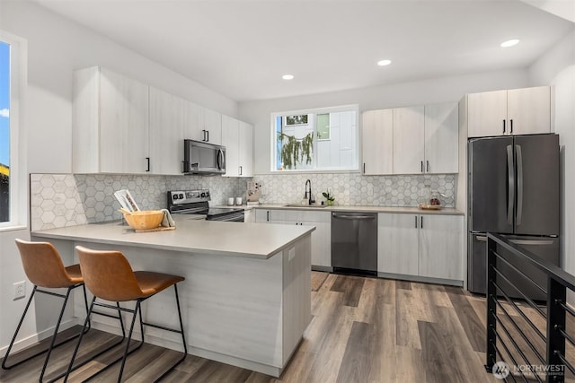 kitchen with stainless steel appliances, a peninsula, dark wood-style flooring, a sink, and a kitchen breakfast bar