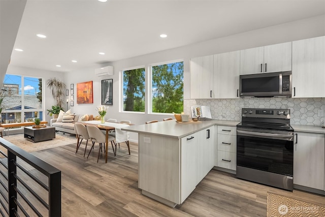 kitchen featuring a peninsula, appliances with stainless steel finishes, a wall unit AC, and light countertops