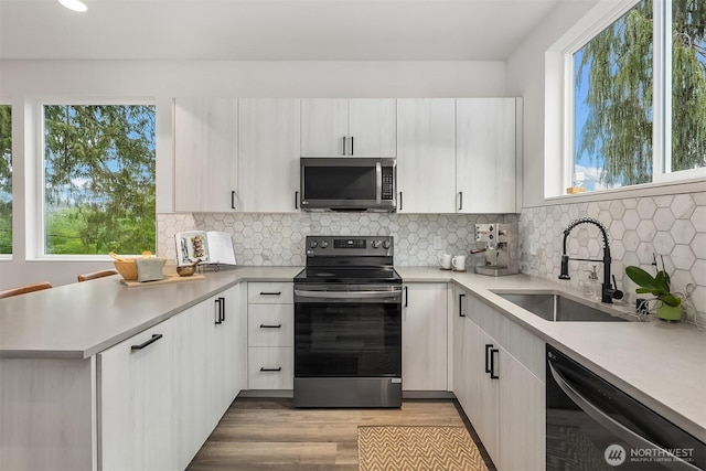 kitchen featuring tasteful backsplash, light countertops, appliances with stainless steel finishes, a sink, and a peninsula