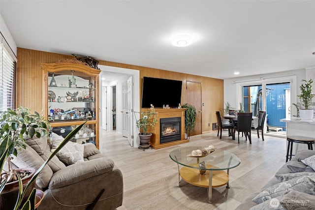 living room with wood walls, a glass covered fireplace, and light wood-style floors