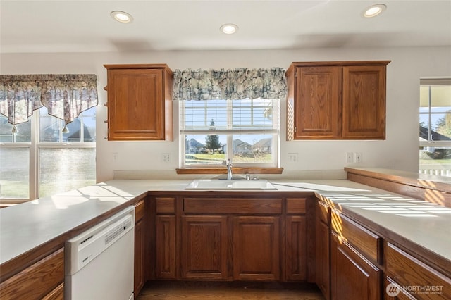 kitchen with white dishwasher, recessed lighting, a sink, light countertops, and brown cabinets