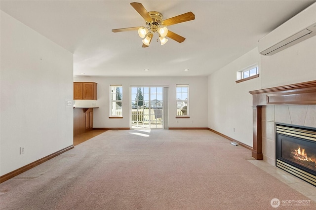 unfurnished living room featuring light colored carpet, a wall mounted AC, a ceiling fan, a tile fireplace, and baseboards