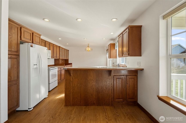 kitchen featuring a peninsula, white appliances, brown cabinets, and wood finished floors