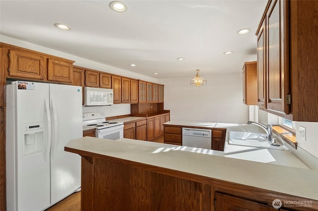 kitchen featuring recessed lighting, a peninsula, white appliances, a sink, and brown cabinetry