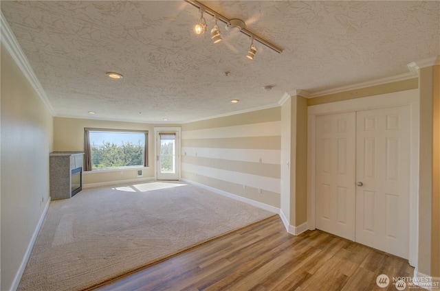 interior space with light wood-style flooring, a textured ceiling, baseboards, and crown molding