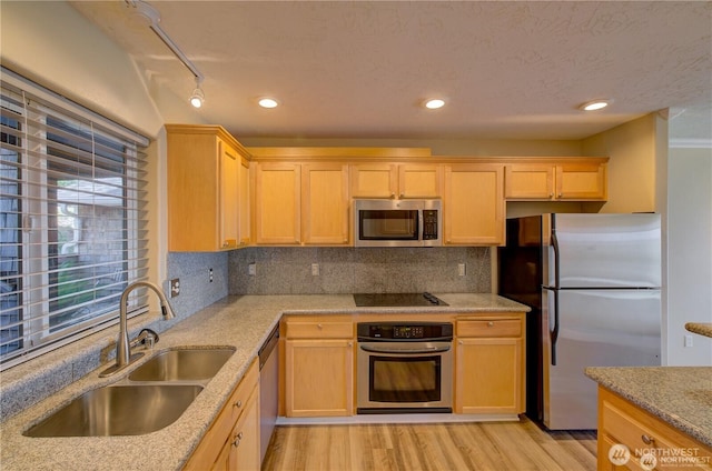 kitchen featuring stainless steel appliances, light brown cabinetry, a sink, and light wood-style flooring