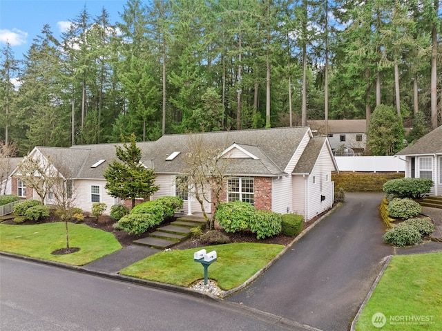 view of front facade with a shingled roof, a front yard, aphalt driveway, and brick siding